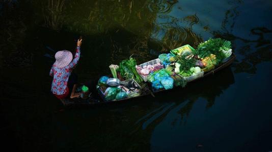 Une vendeuse se dirige vers le marché pour y vendre ses légumes. L'impression que l'eau est en train de dormir. ©La Mo